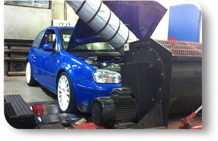 Blauer VW Golf auf dem Rollenprüfstand in der Werkstatt, Motorhaube geöffnet, vor dem Fahrzeug ein großes Kühlluftgebläse