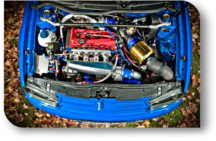 Offener Motorraum eines blauen, getunten Autos mit rotem Ventildeckel, Ansaugsystem und goldfarbenem Sportluftfilter
